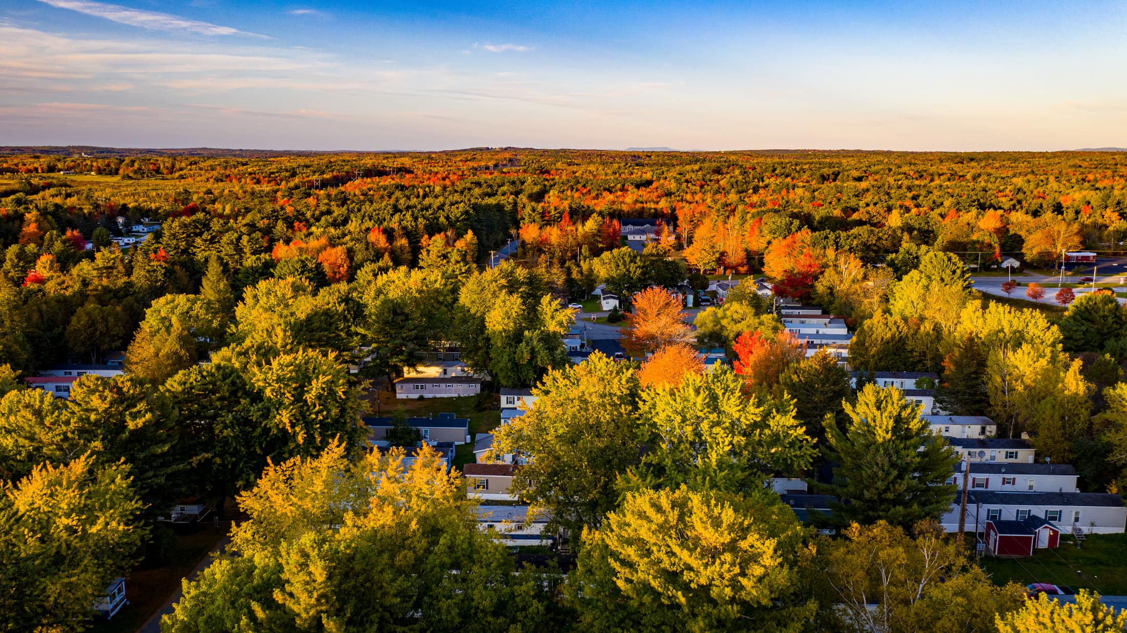 Aerial view of Cedar Haven manufactured home community surrounded by autumn forest at sunset in Holden, Maine